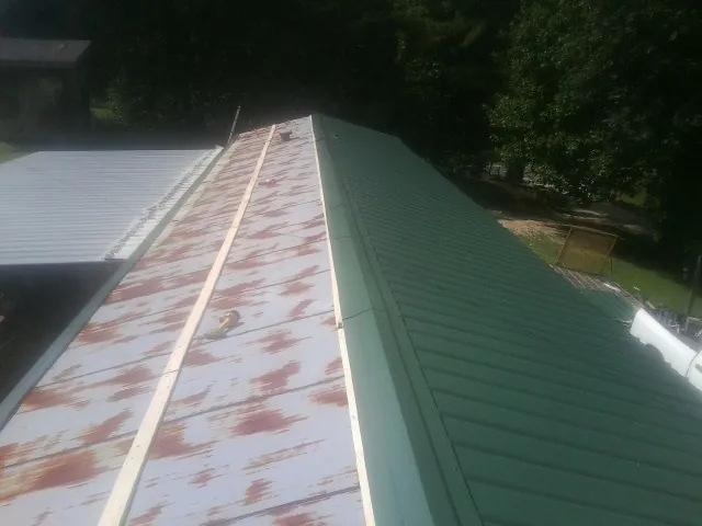 Old rusted panels beside newly installed green metal roofing — Wind Damage Roof Repair by Roofing Brothers in Glenwood