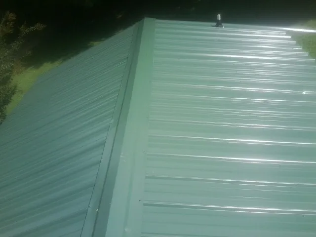 New green metal panels meeting at the ridge of a roof — Flat Roof Repair work by our crew in Glenwood
